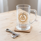 Celtic triquetra glass beer tankard on its cork coaster with the axe-shaped metal bottle opener.